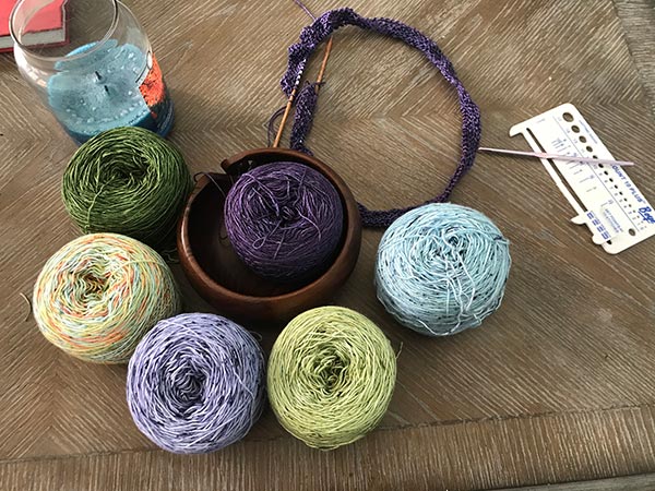 Yarn in six colors, purple, lighter purple, blue, green, green with orange flecks, and emerald green.